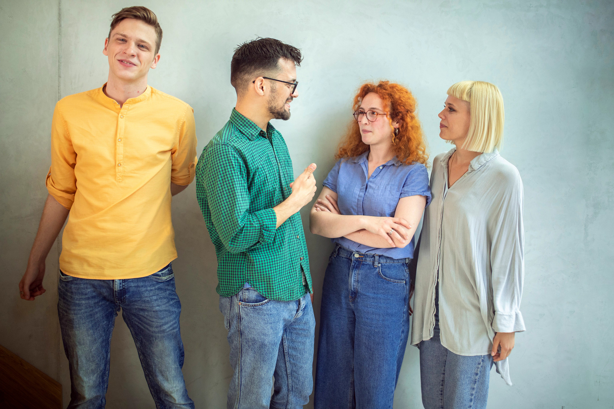 Two men and two women hanging out and chatting in front of a wall