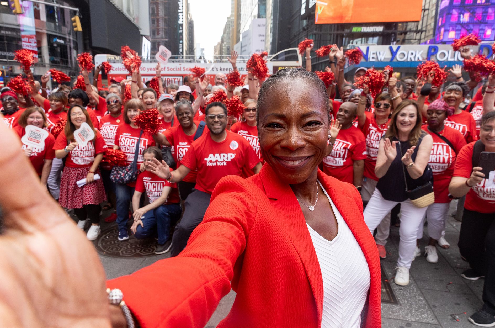 Dr. Myechia Minter-Jordan in Times Square a woman in red blazer and white shirt stands in front of a crowd wearing red a a r p shirts