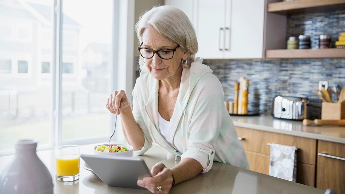 woman in kitchen eating while on tablet woman in kitchen eating while on tablet