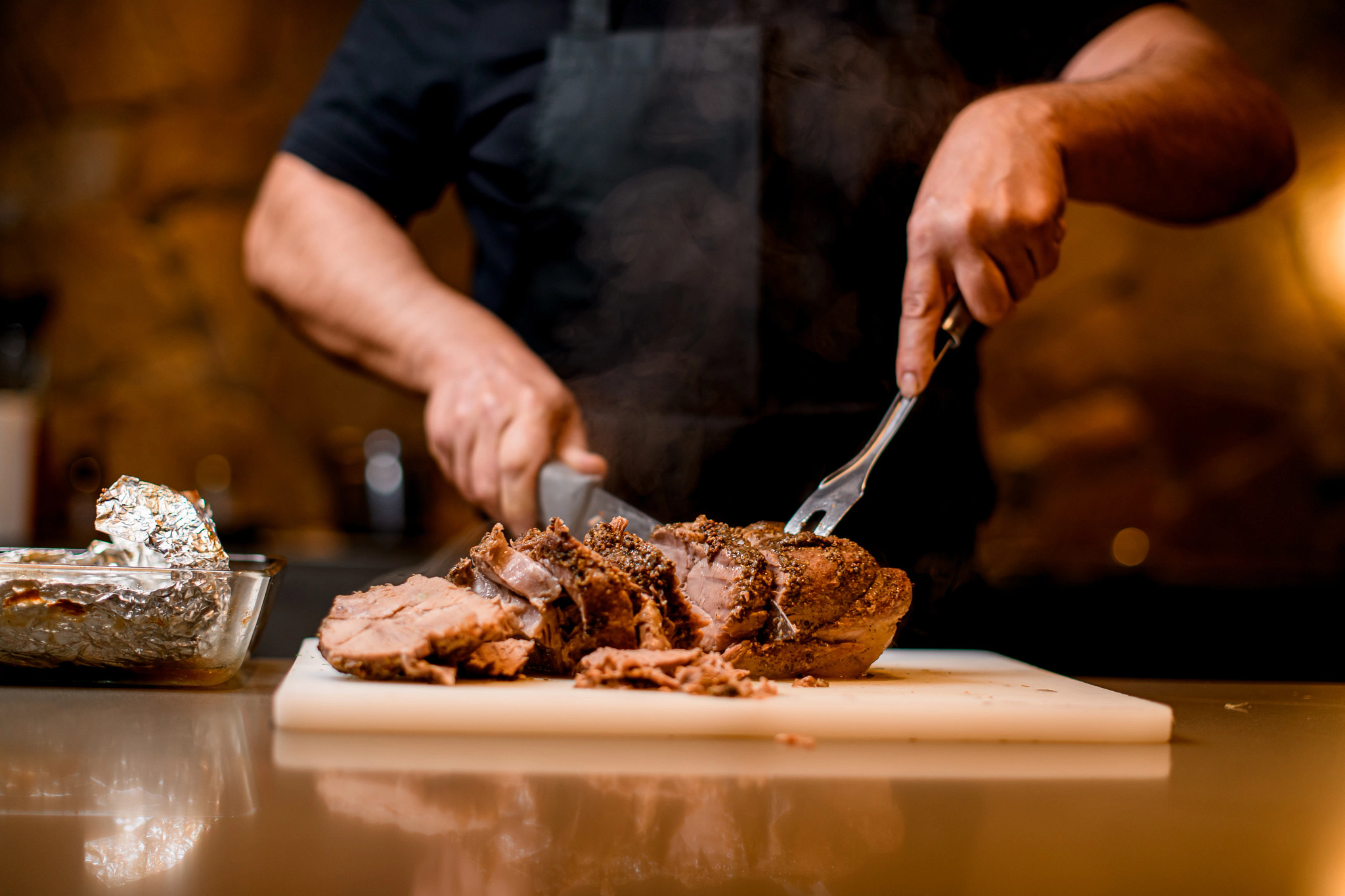A chef carves up a large hunk of barbecue meat on a plastic cutting board