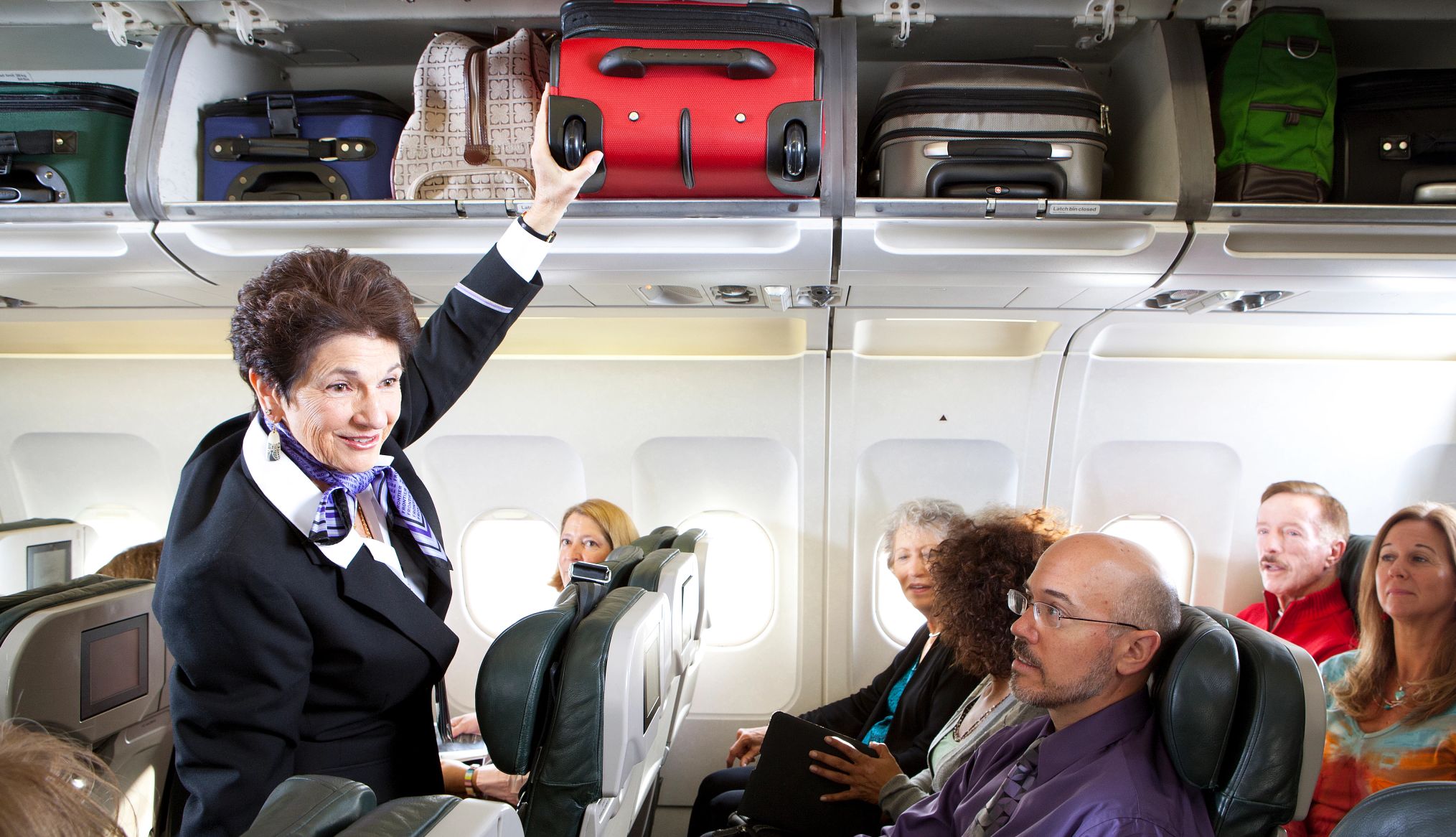 a woman flight attendant is putting luggage in an overhead bin