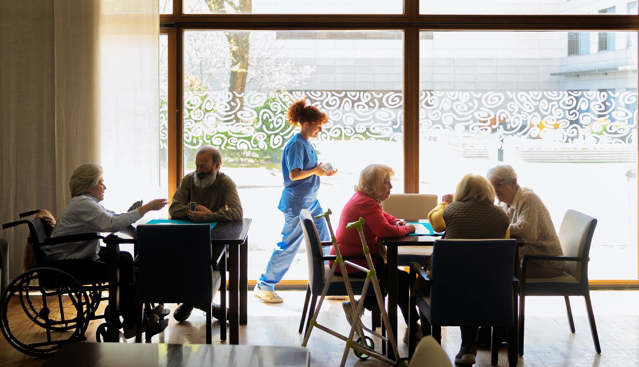 AARP Pushes Back on Effort to Delay Federal Nursing Home Staffing Standards Compassionate nurse helping senior residents with daily activities in retirement home communal area, offering personalized care and companionship