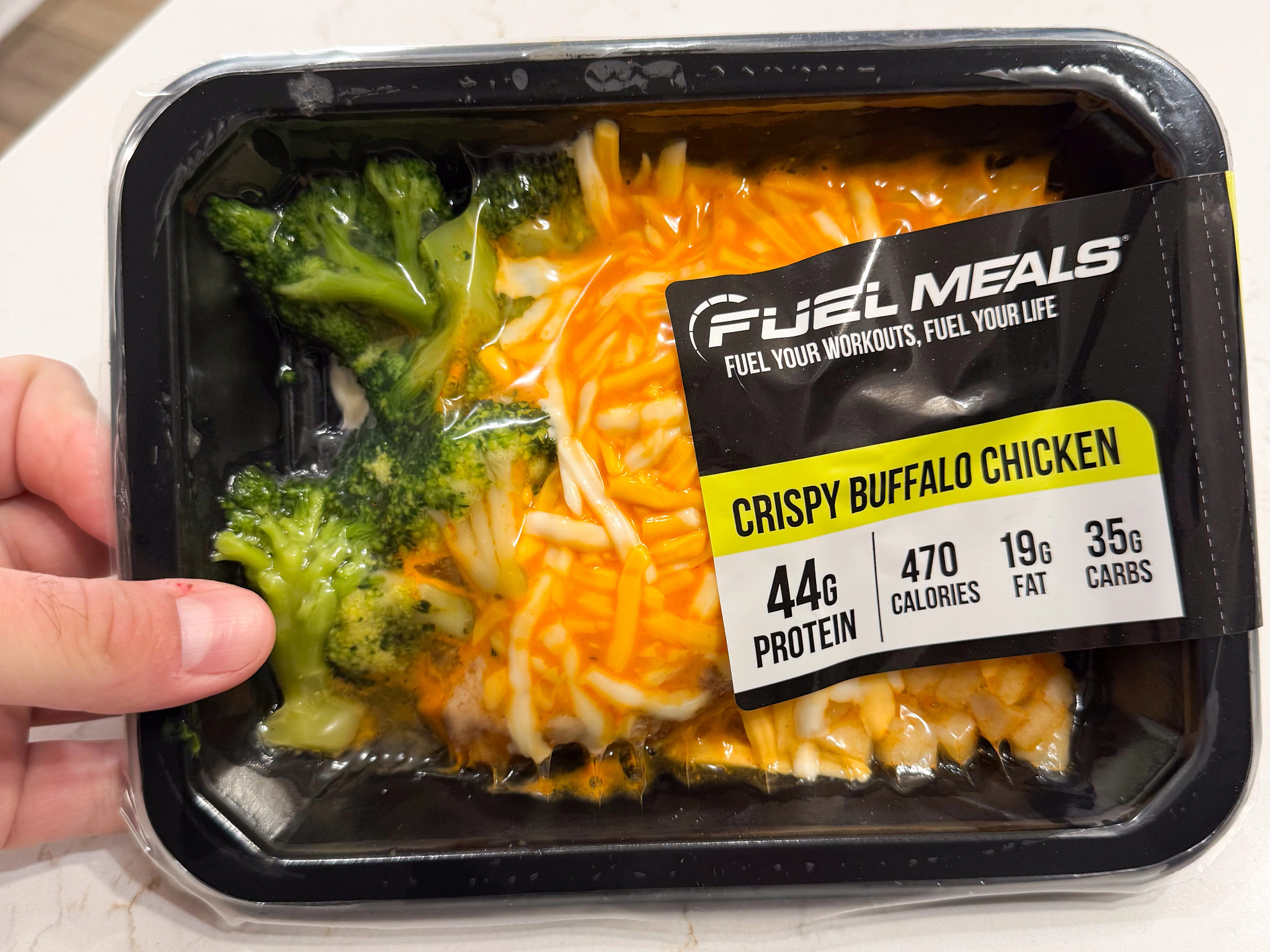 A meal with broccoli and shreds of cheese vacuum sealed into a black container with a fuel meal info label on the front