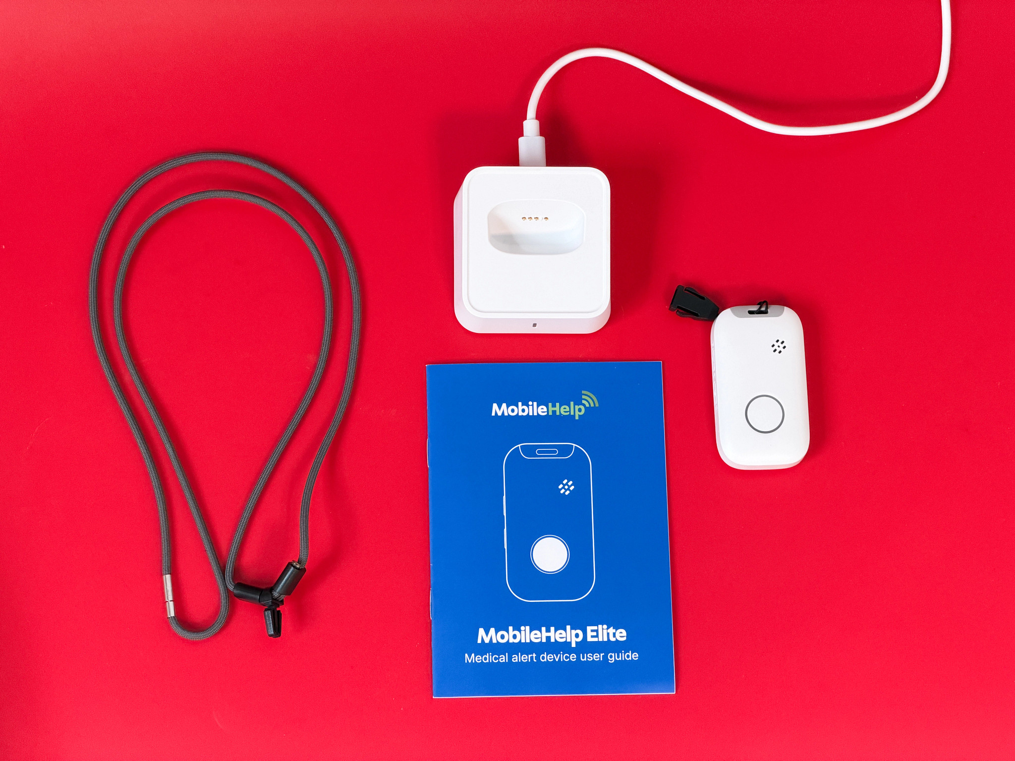 The MobileHelp Elite components and manual on a red background