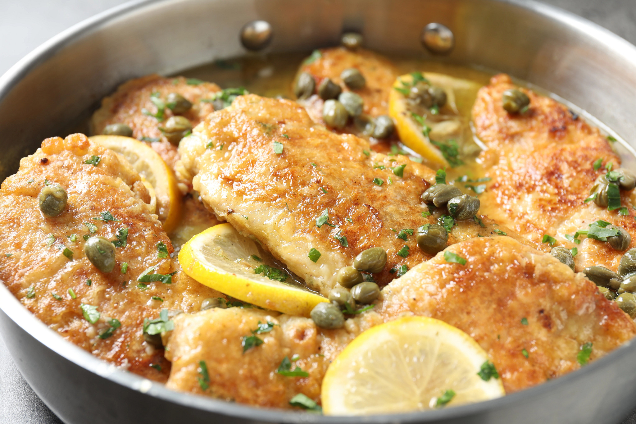 Close-up of golden chicken piccata cooked in a lemon and caper sauce in a skillet