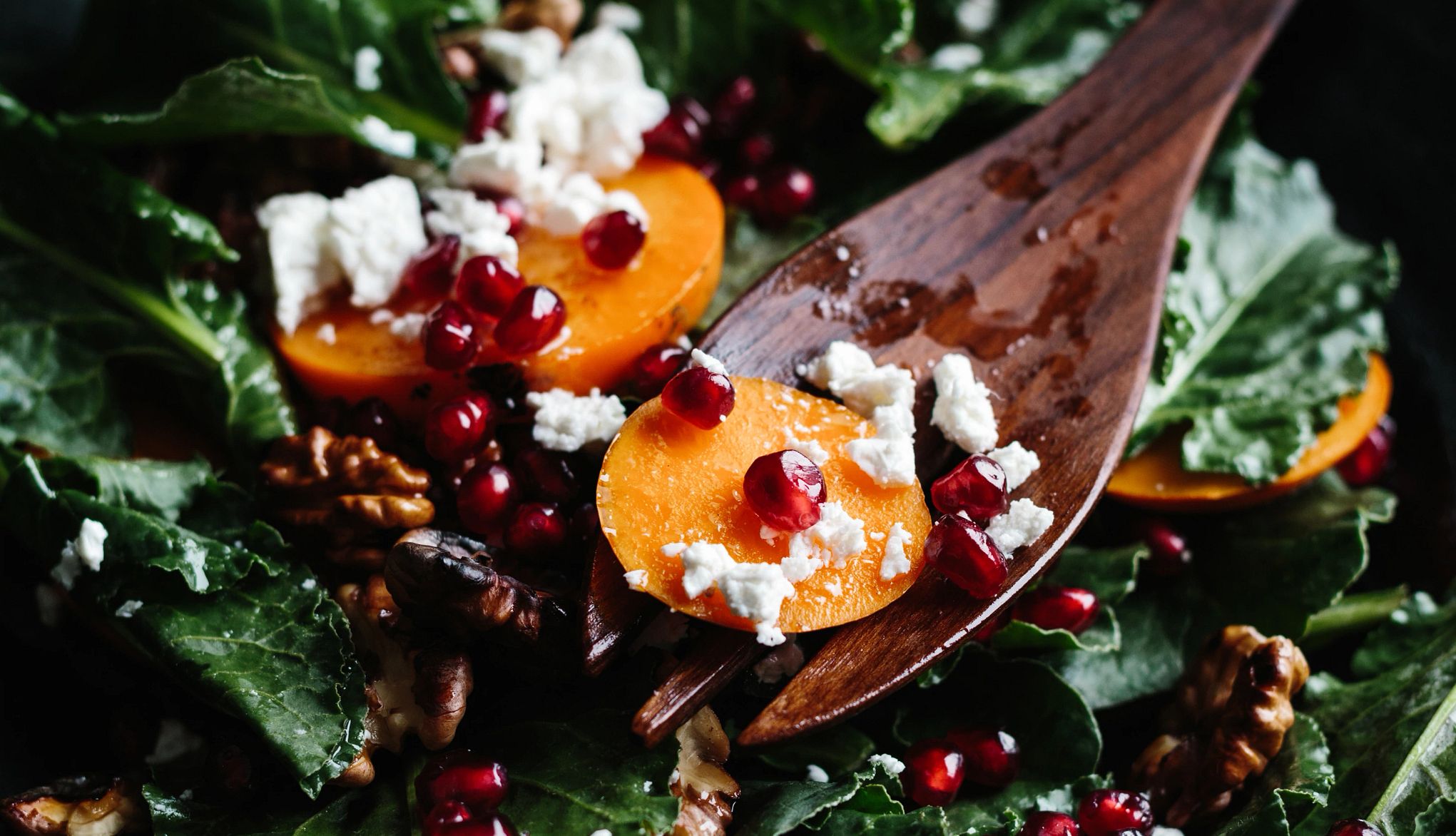 Healthy Fall Foods sweet potatoes, goat cheese, pomegranate seeds and walnuts in a salad with wooden spoon