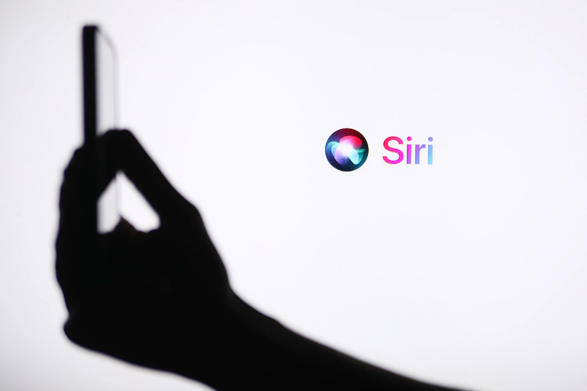 a photo shows a person holding an iphone with a siri logo in the background