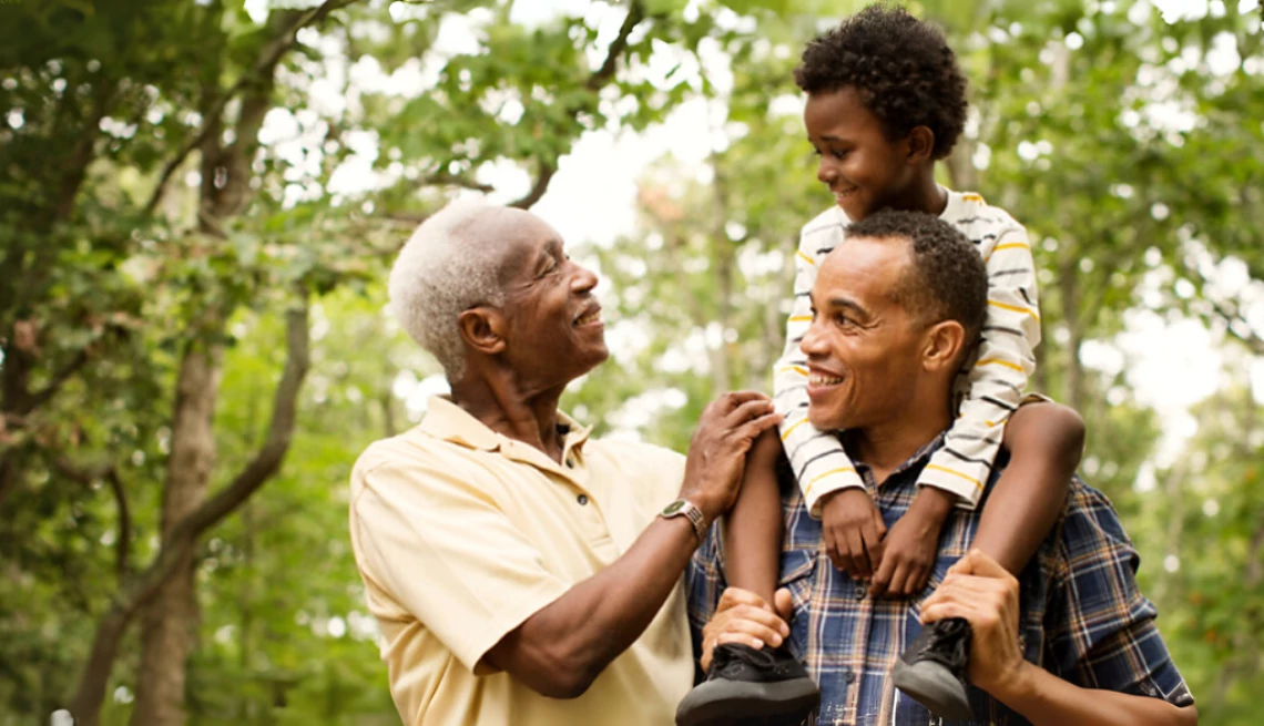 A dad carrying his son on his shoulders with the boy's grandfather walking beside them in a wooded area