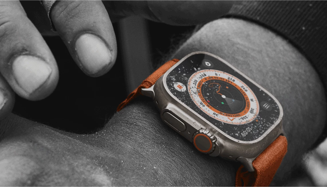 Consumer Cellular hands and arm wearing a smartwatch with sand on it and orange strap