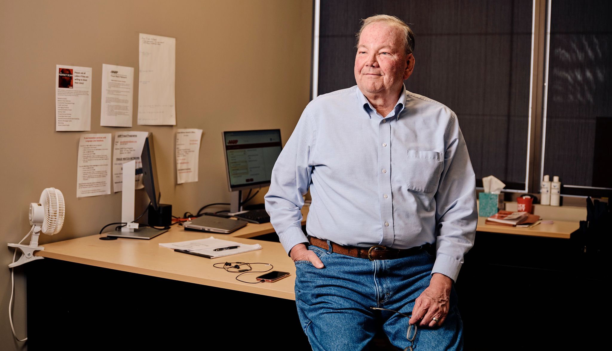 Volunteers at the AARP Fraud Watch Network Helpline help victims who call in a man stands in front of a desk with one hand in his pocket
