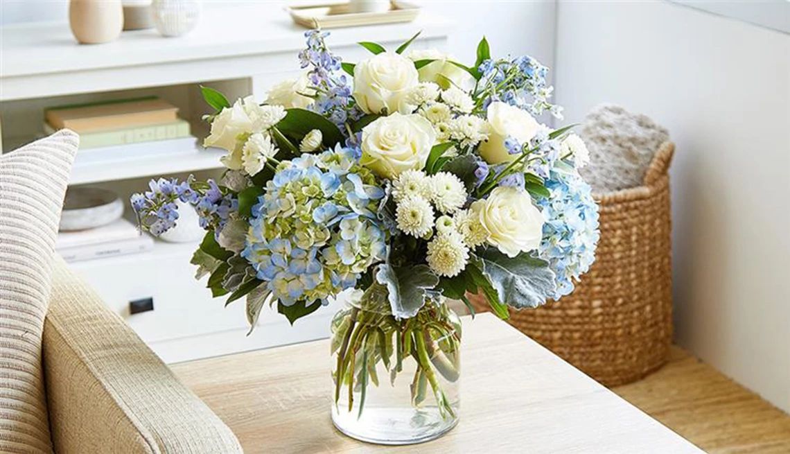 Bouquet of white and blue flowers in glass vase sitting on side table in living room