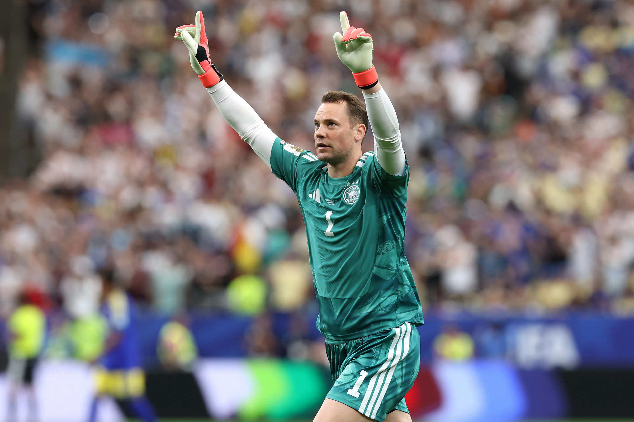 manuel neuer raising his arms on a soccer field, with a serious expression