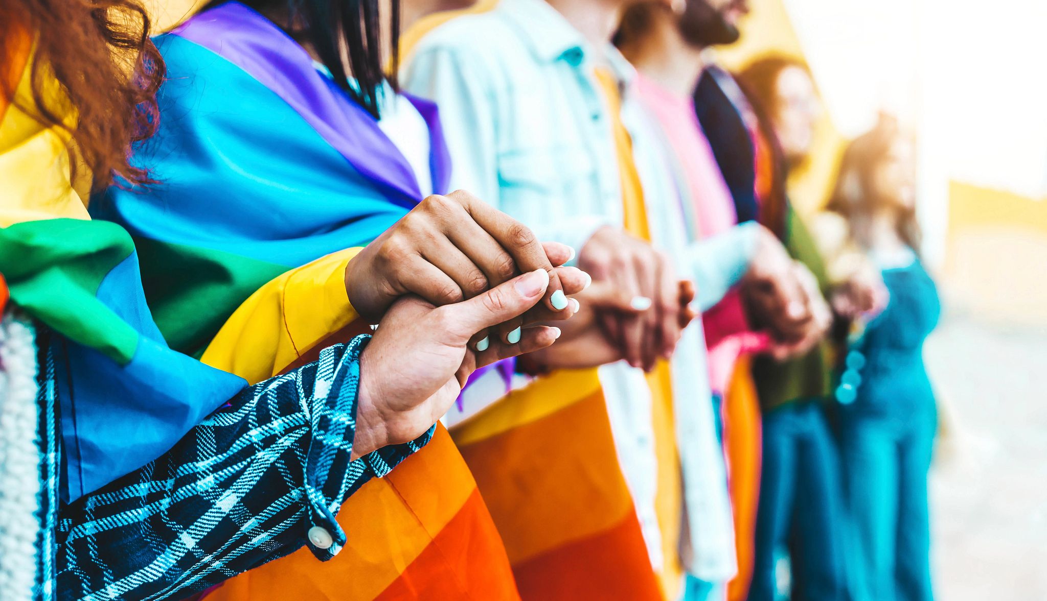 A group of people holding hands, draped in LGBTQIA+ flags A group of people holding hands, draped in LGBTQIA+ flags