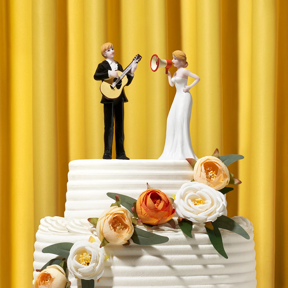 Wedding cake topper featuring a guitar-playing groom and a megaphone-holding bride