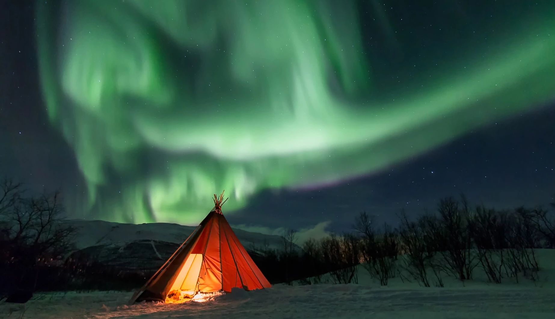 Sweden’s Abisko National Park is a great viewing location. a tent lit up at night with the Northern Lights in the sky