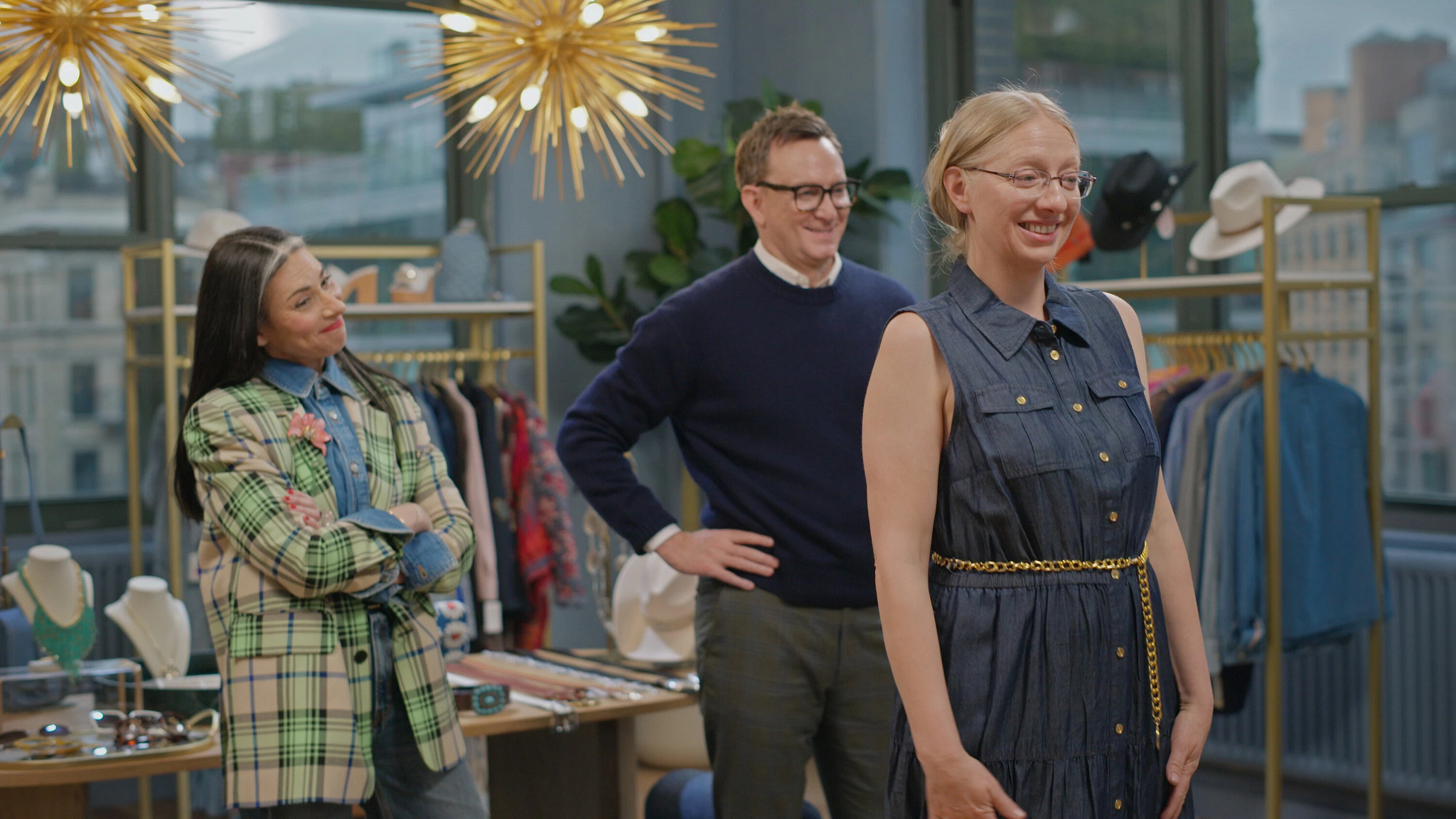 a participant smiling while trying on an outfit as stacy london and clinton kelly look on