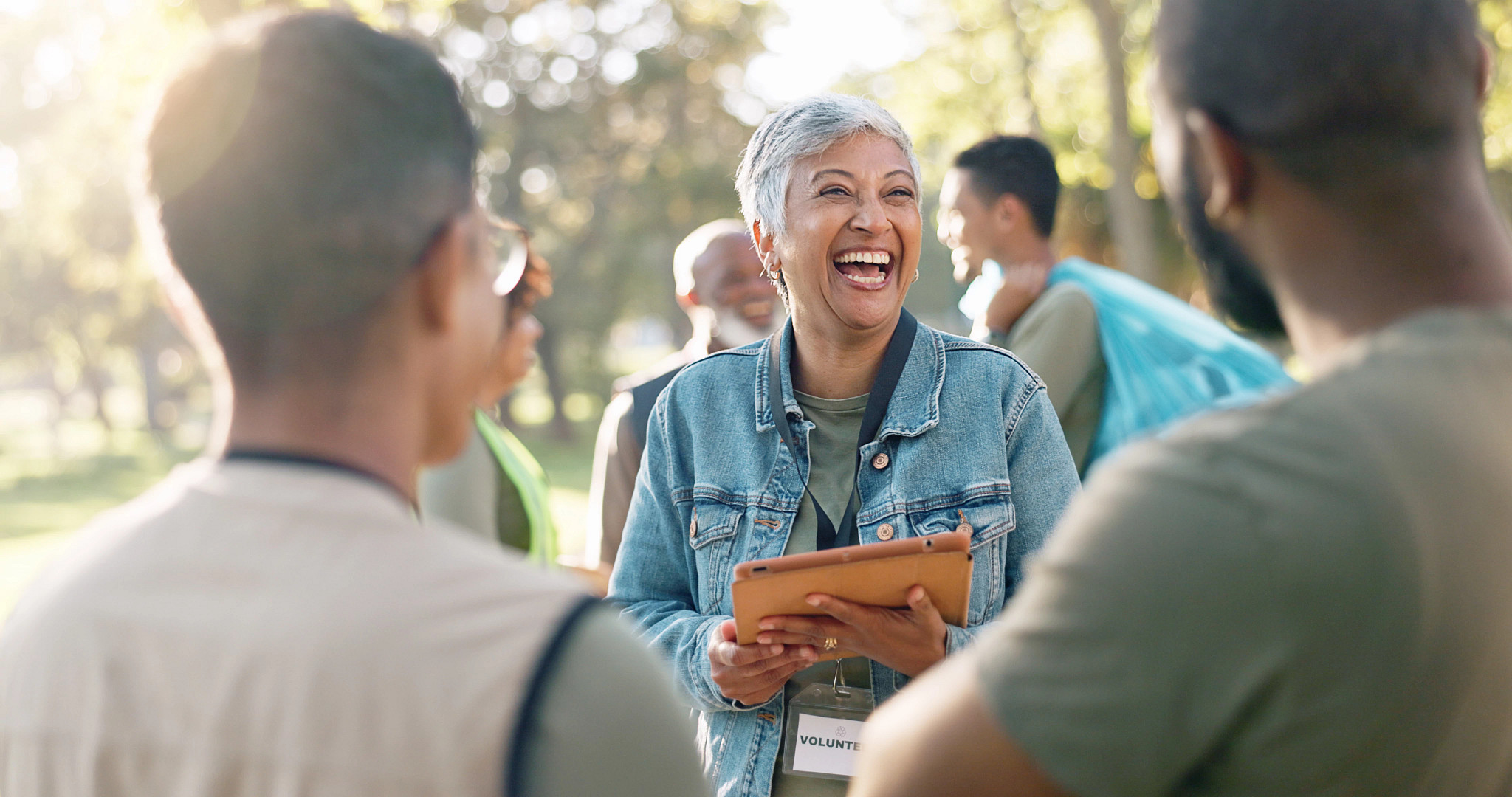 a laughing woman holding a clipboard talking to two volunteers