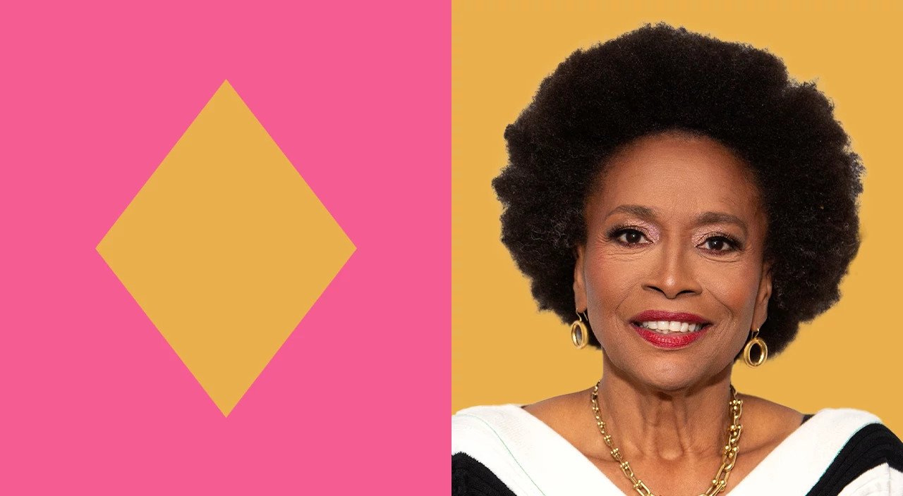 Jenifer Lewis with natural curly afro hairstyle against a bright yellow background wearing gold hoop earrings