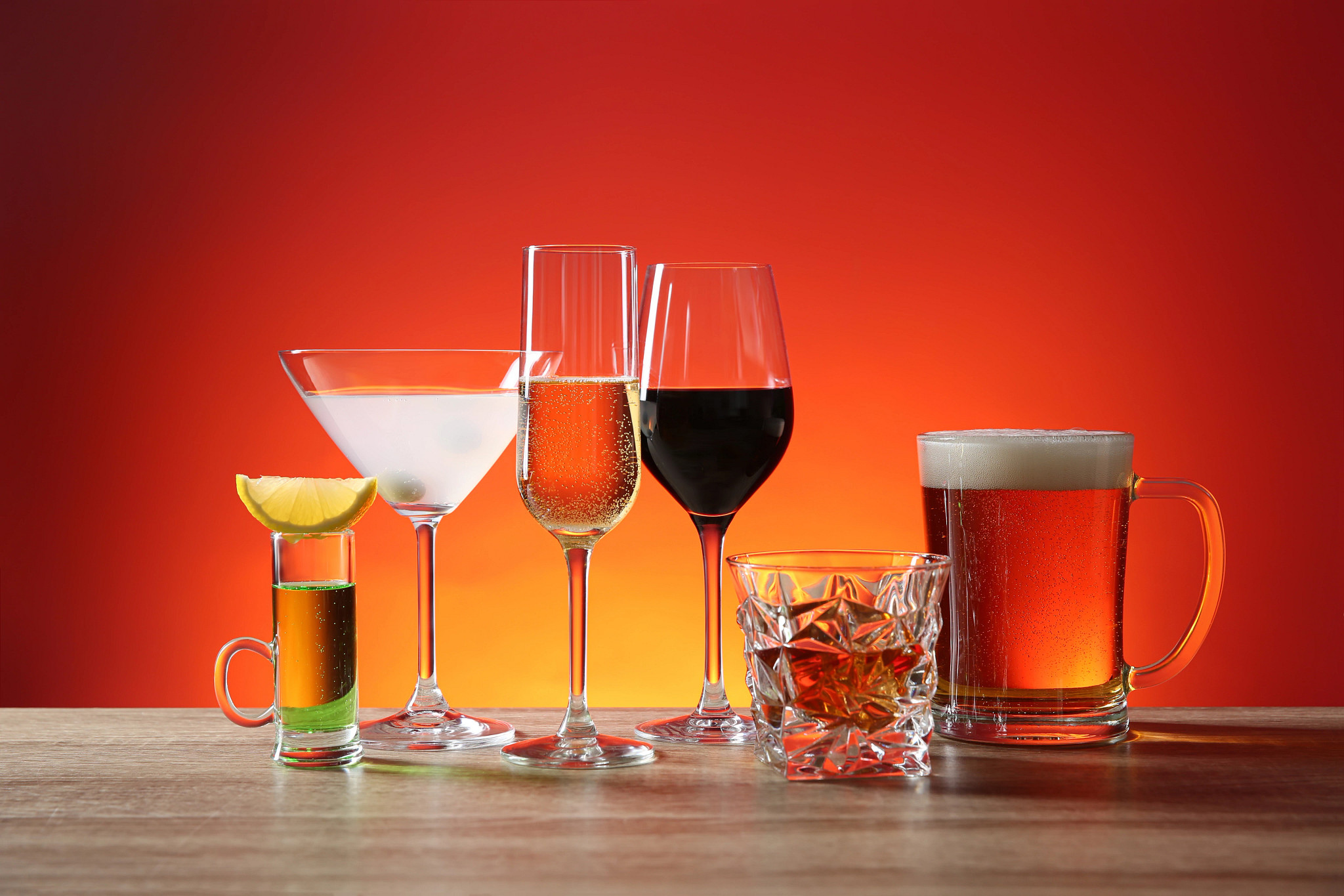 Various alcoholic drinks, including a shot glass, martini, champagne, red wine, whiskey on the rocks, and a mug of beer, lined up against a red gradient background.