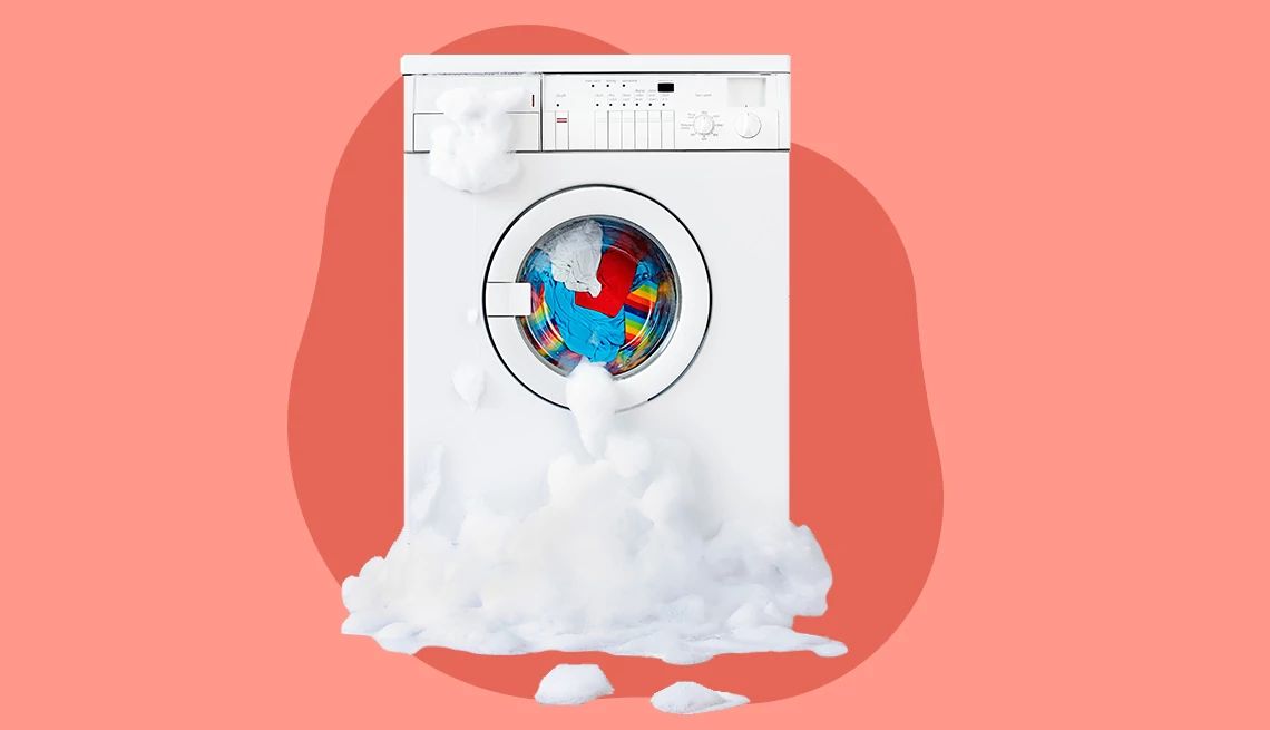 washing machine filled with colorful clothes with soap suds spilling out onto the floor