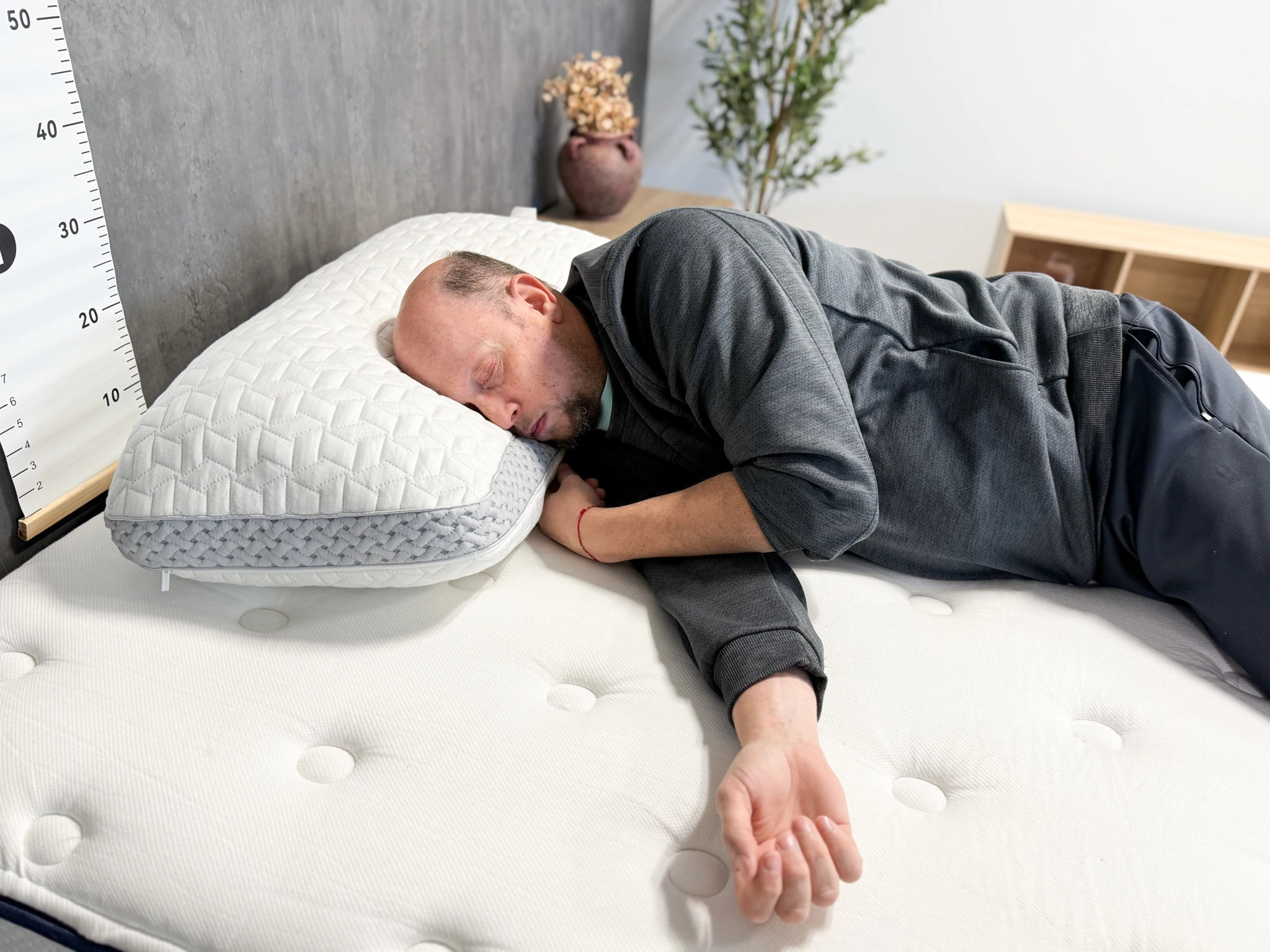 A man lying on his side on a bed with his head resting on the Luxome LAYR Pillow