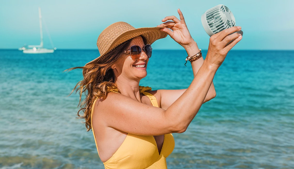 Woman at the beach A smiling woman wearing a sun hat and yellow swimsuit at the beach while holding a fan to her face