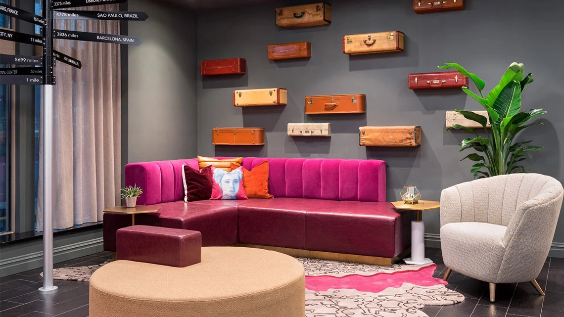 View of colorful lounge at TRYP hotel property, pink bench, wood shelves, green plant, white chair