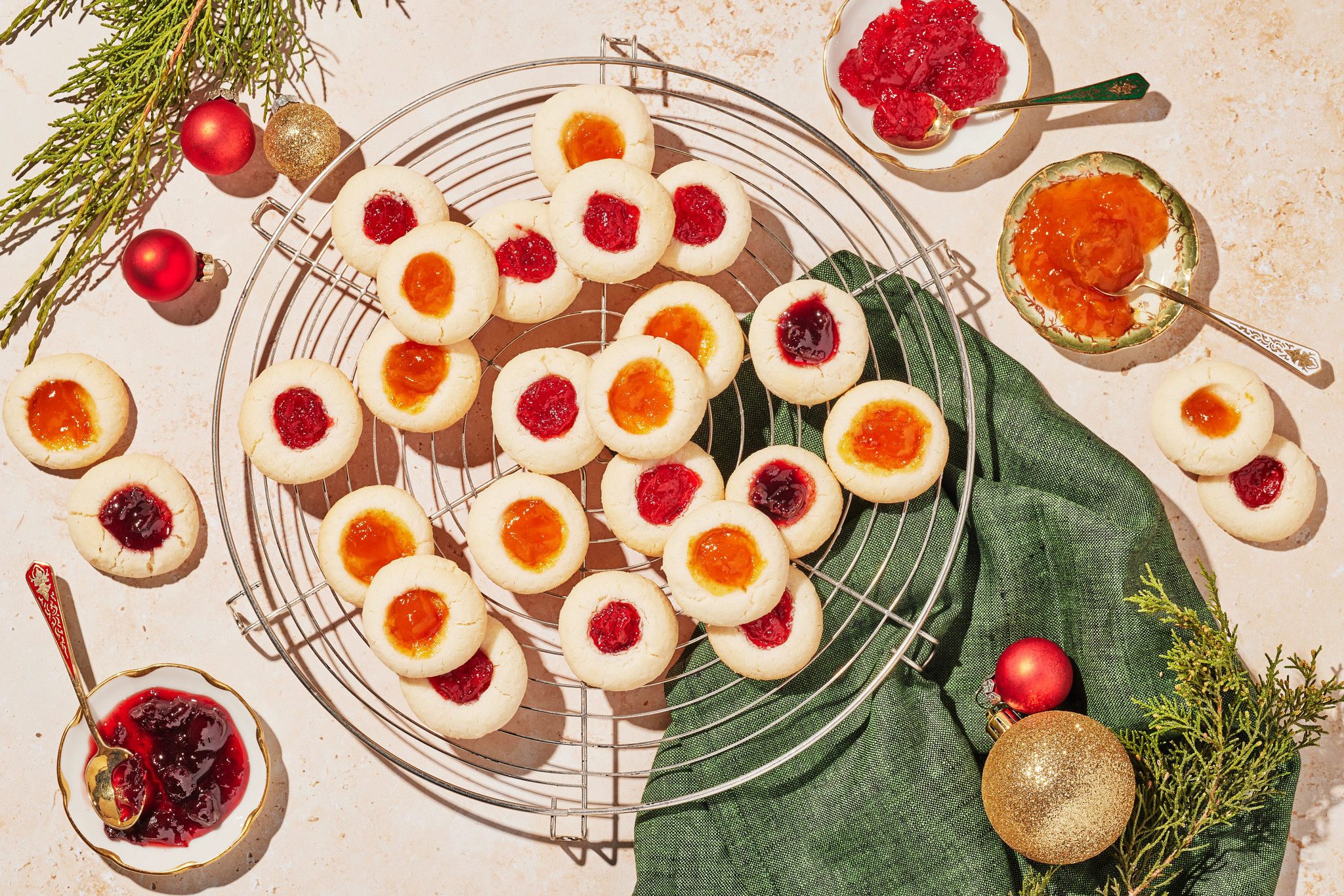 Homemade Christmas thumbprint cookies with jam centers cooling on a wire rack surrounded by festive decorations