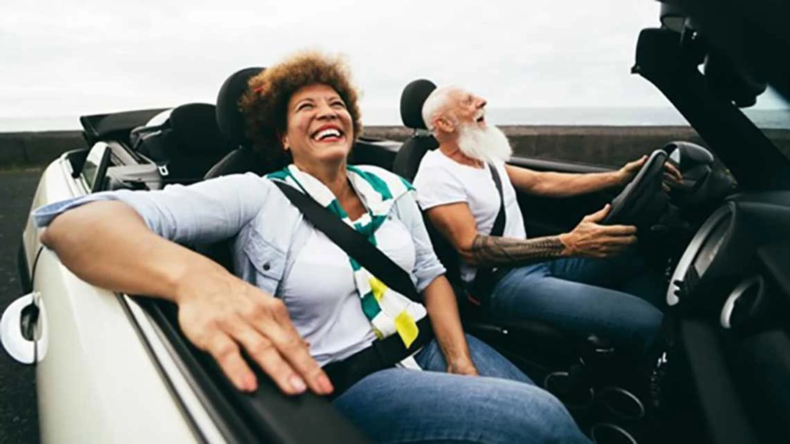 Expedia Car Rental Discounts for AARP Members man driving and woman in passenger seat of convertible car smiling on cloudy day