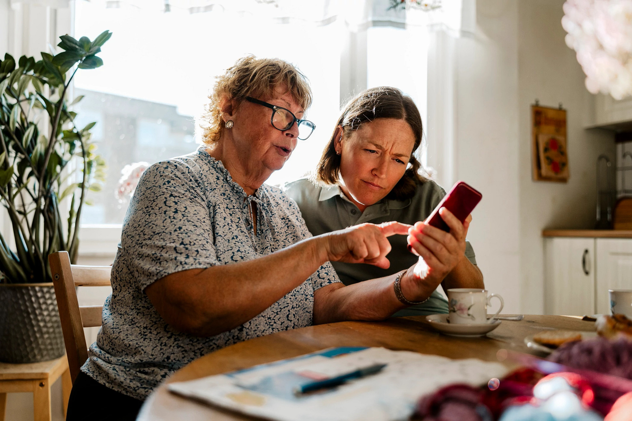 Senior woman sharing smart phone with female helper sitting at home