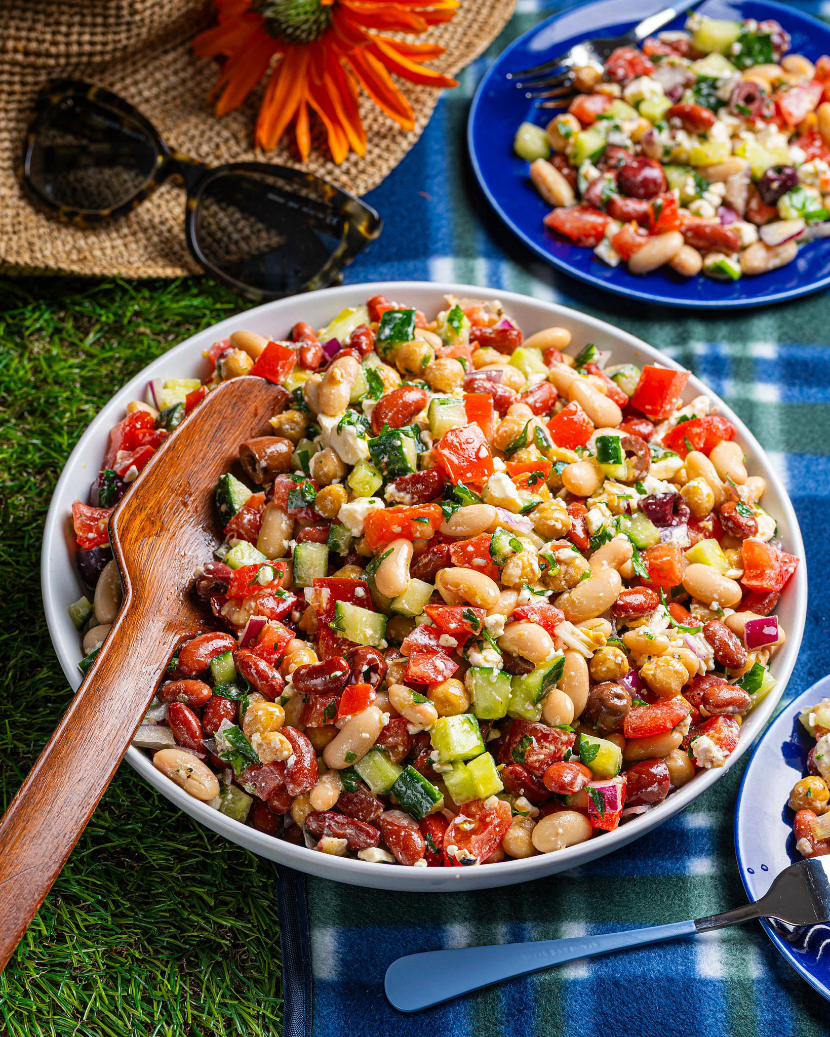 A three-bean salad served on a picnic blanket, paired with summer accessories like sunglasses and a sun hat