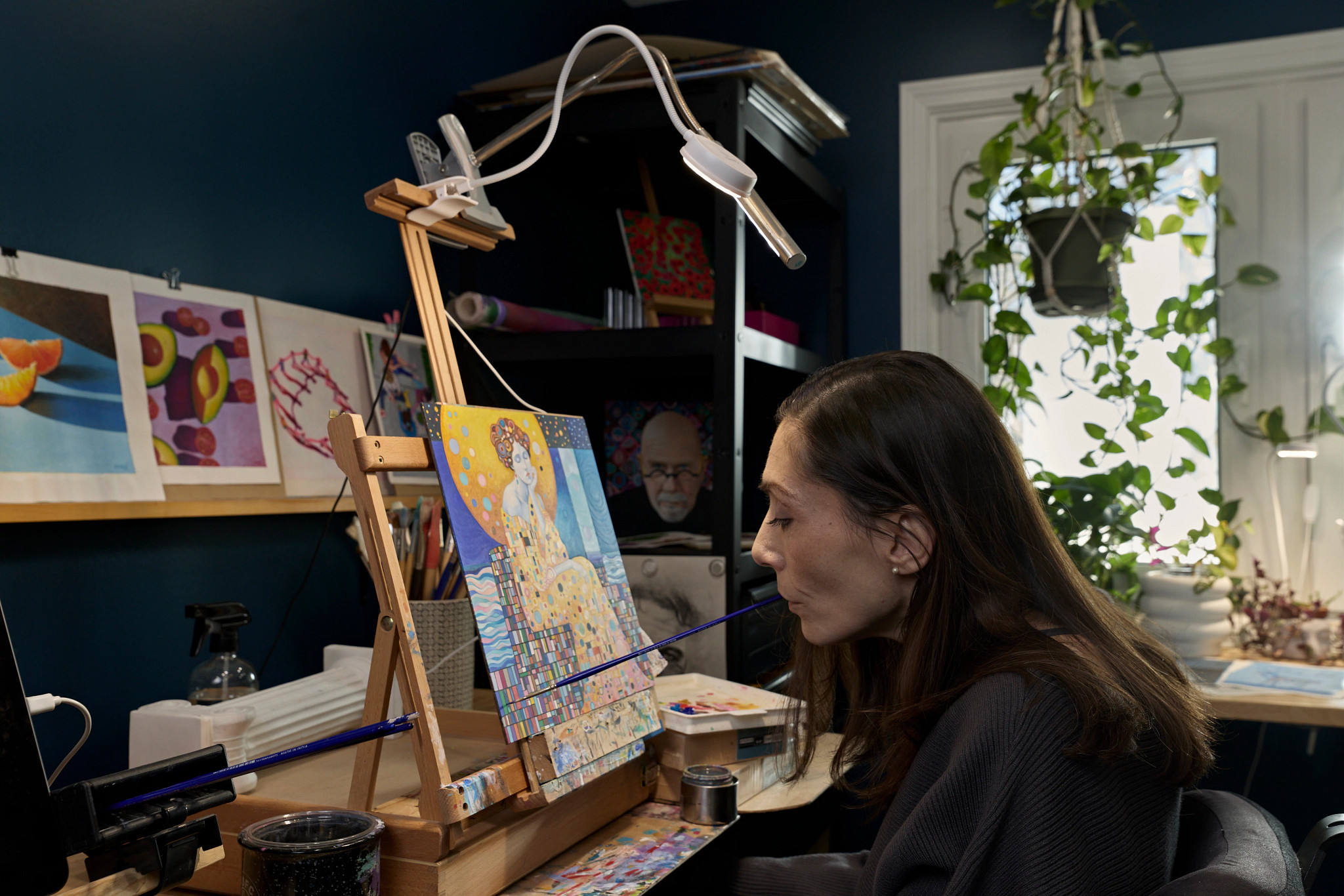 mariam pare holding a paintbrush in her mouth as she works on a painting