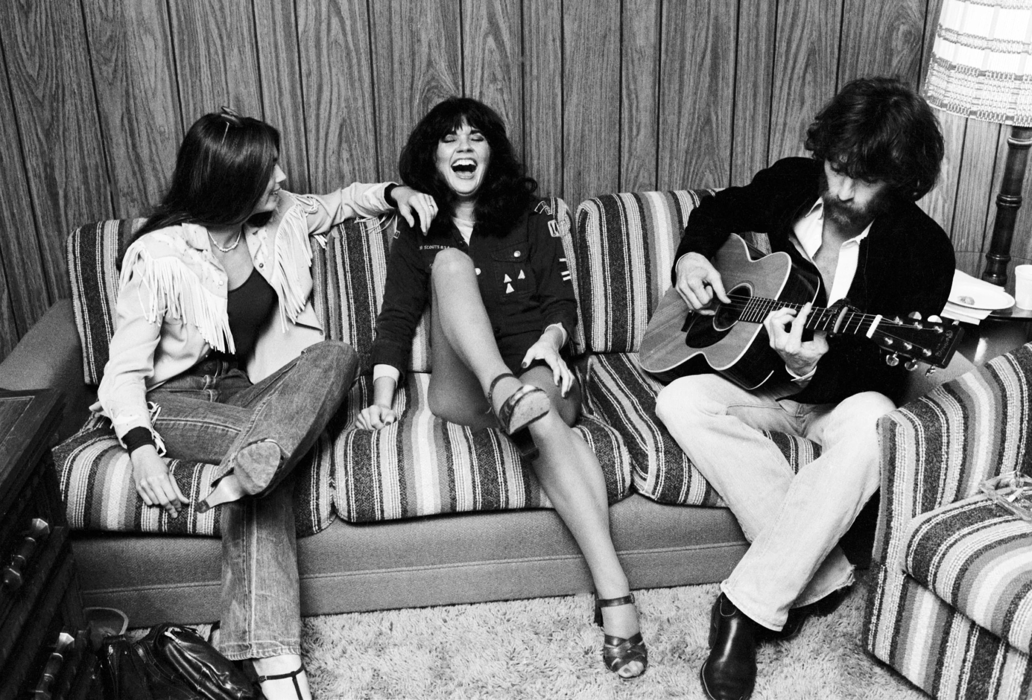 JD Souther plays an acoustic guitar on a couch beside Emmylou Harris and Linda Ronstadt in Los Angeles
