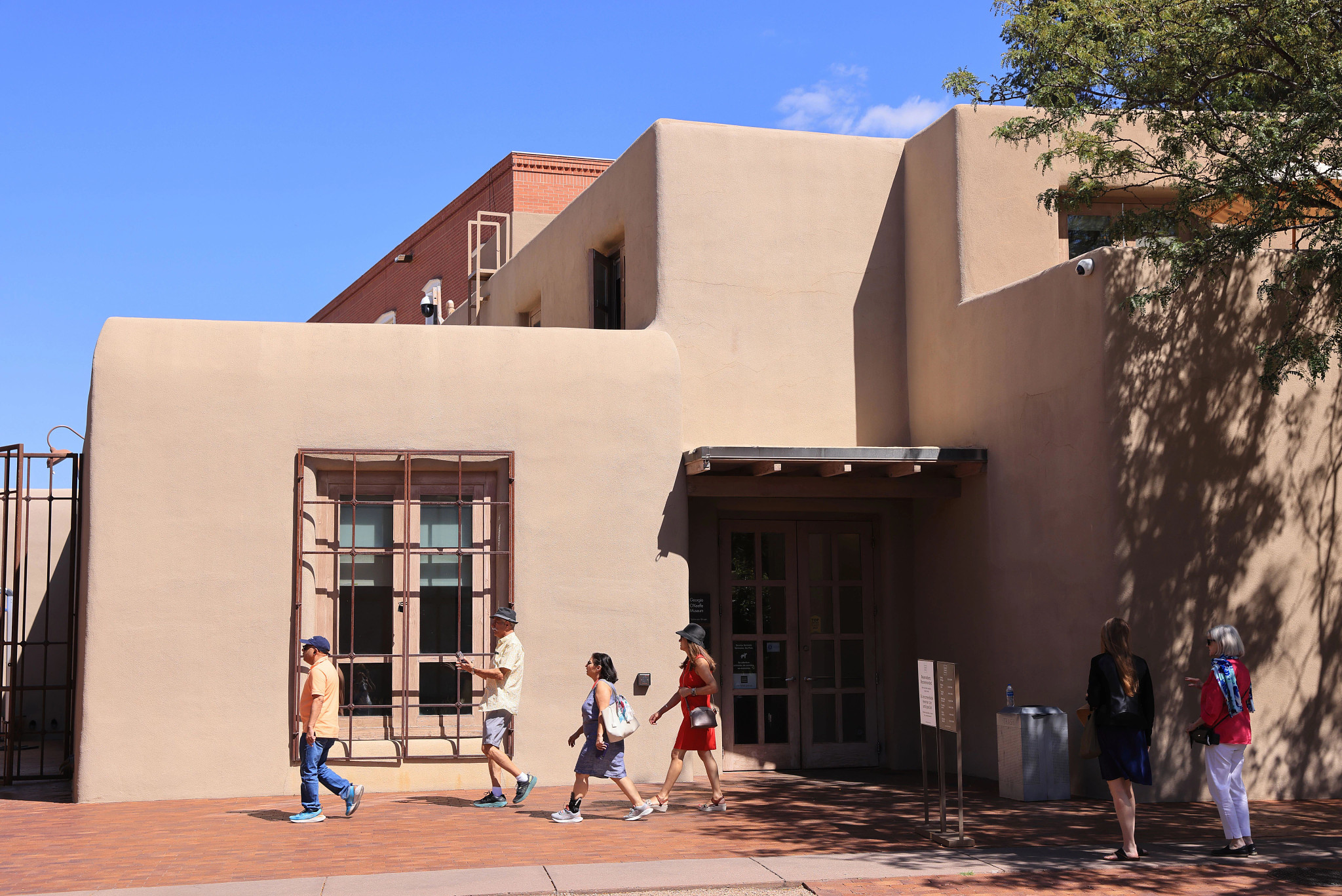 visitors walk past the outside of a pueblo style building