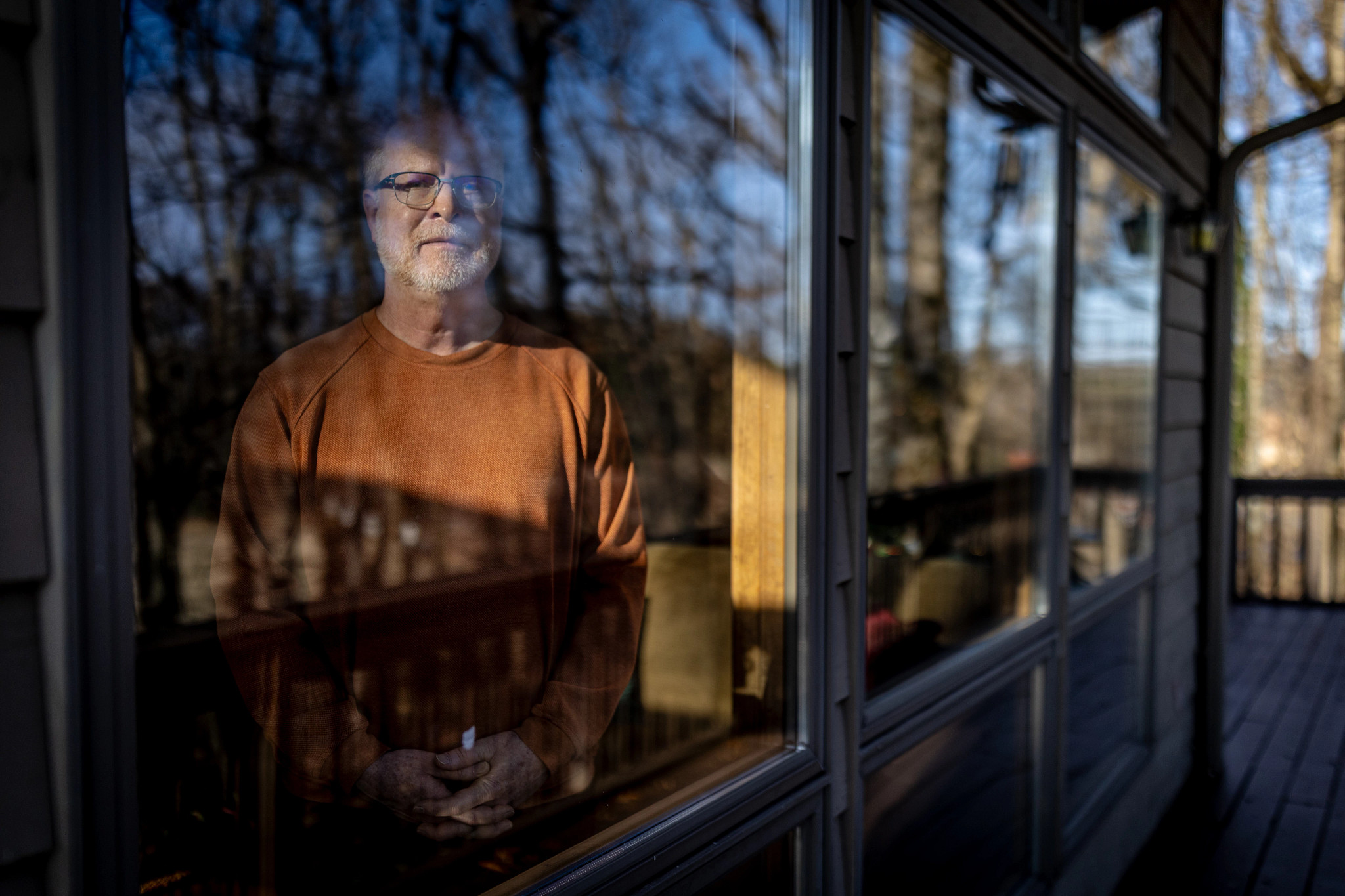 a man stands at a window, seen from outside the home