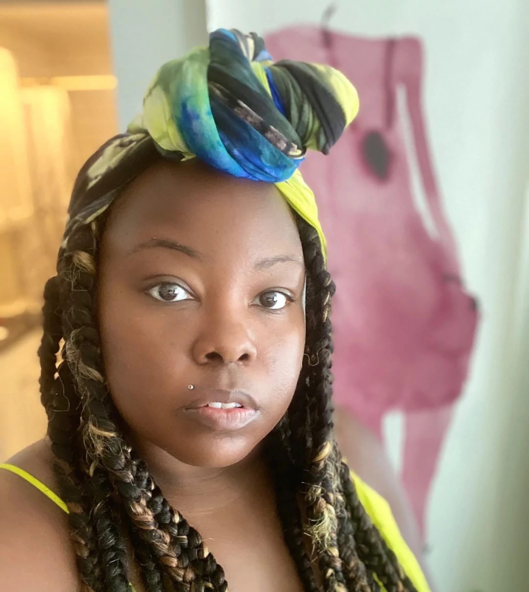 A person with braided hair and a colorful headscarf looks toward the camera in an indoor setting