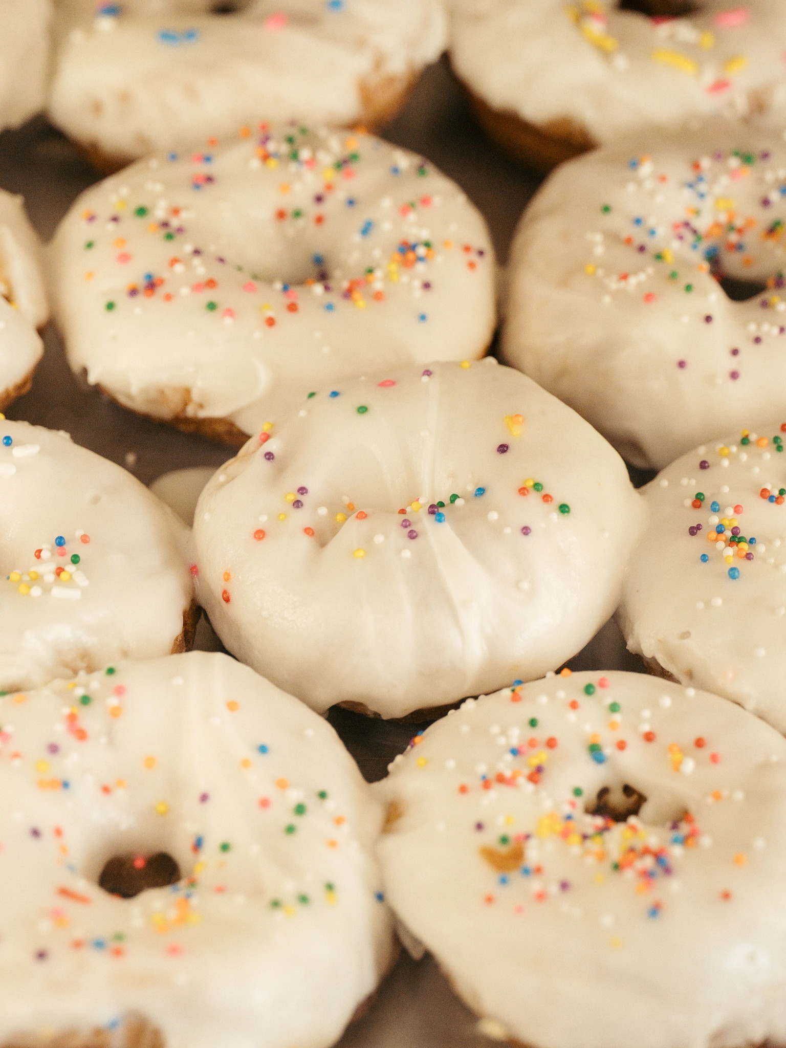Close-up of freshly baked doughnut topped with smooth white icing and rainbow sprinkles