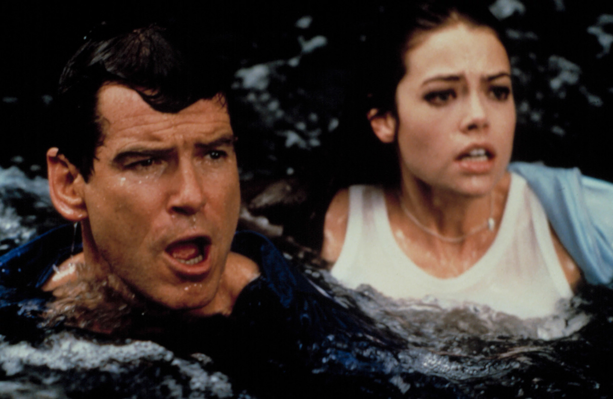 Close-up shot of Denise and Pierce Brosnan partially submerged in dark, murky water