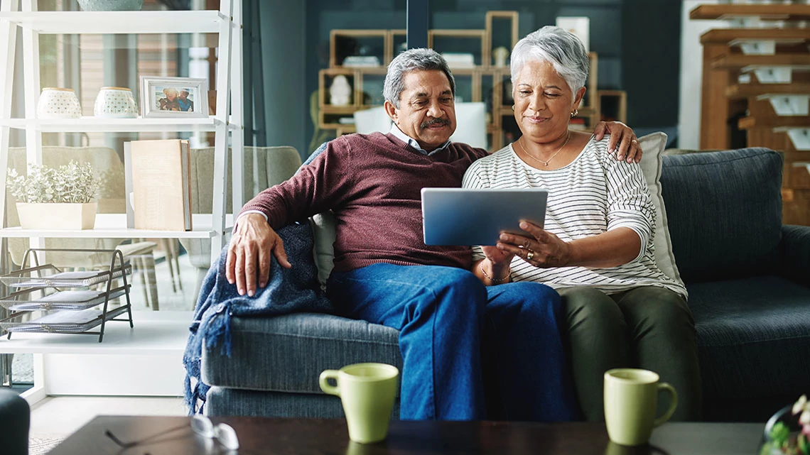 man and woman sitting on couch viewing a tablet