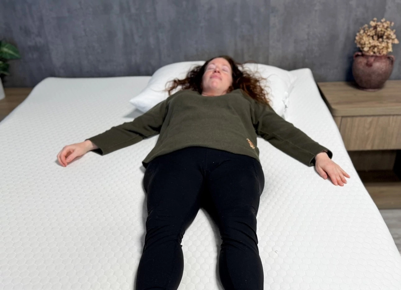 Woman lies on her back in bed with her eyes closed and arms splayed at her side