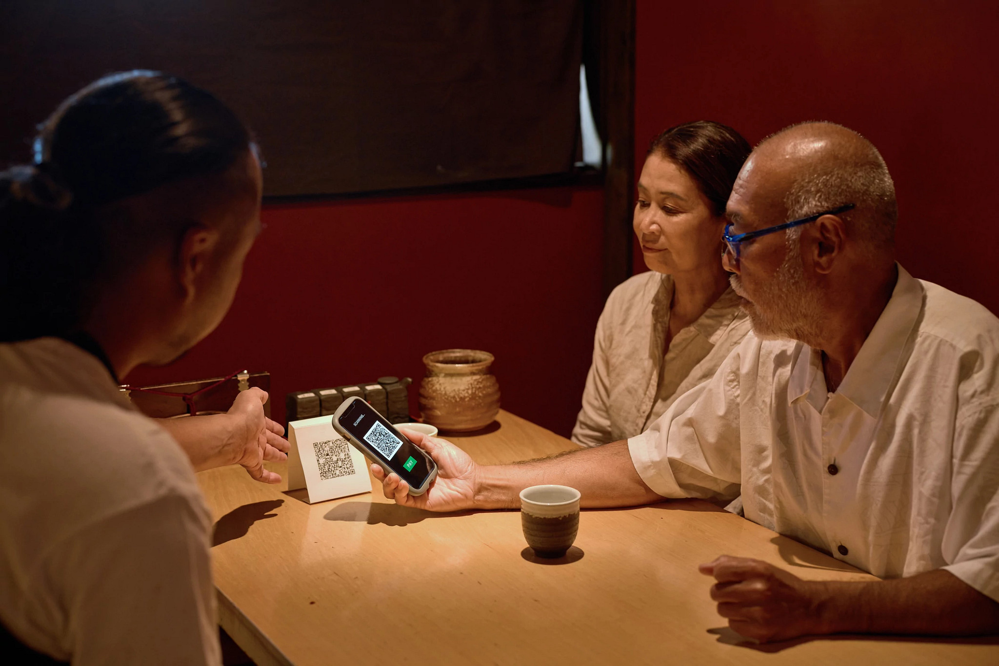 Senior couple reading QR code on smartphone at locally loved yakitori restaurant