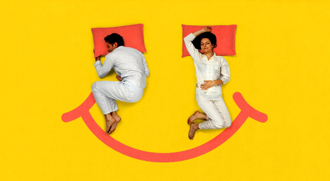 a photo illustration shows a couple in pajamas on a yellow background as if in bed. The man is rolled over away from the woman. Their two orange pillows make the eyes of a happy face, with the mouth drawn in orange