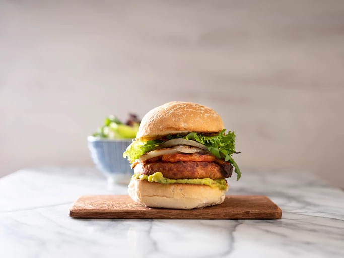 Vegan burger on a chopping board. Bowl of salad in the background