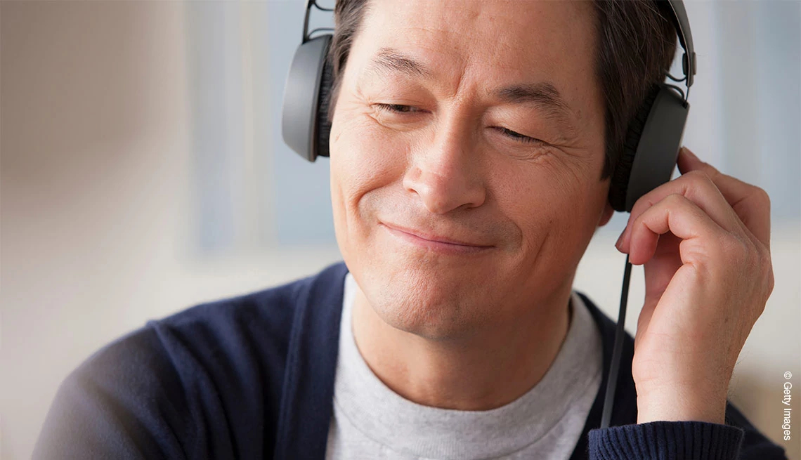 Mature man wearing headphones, smiling, one hand touching right ear phone