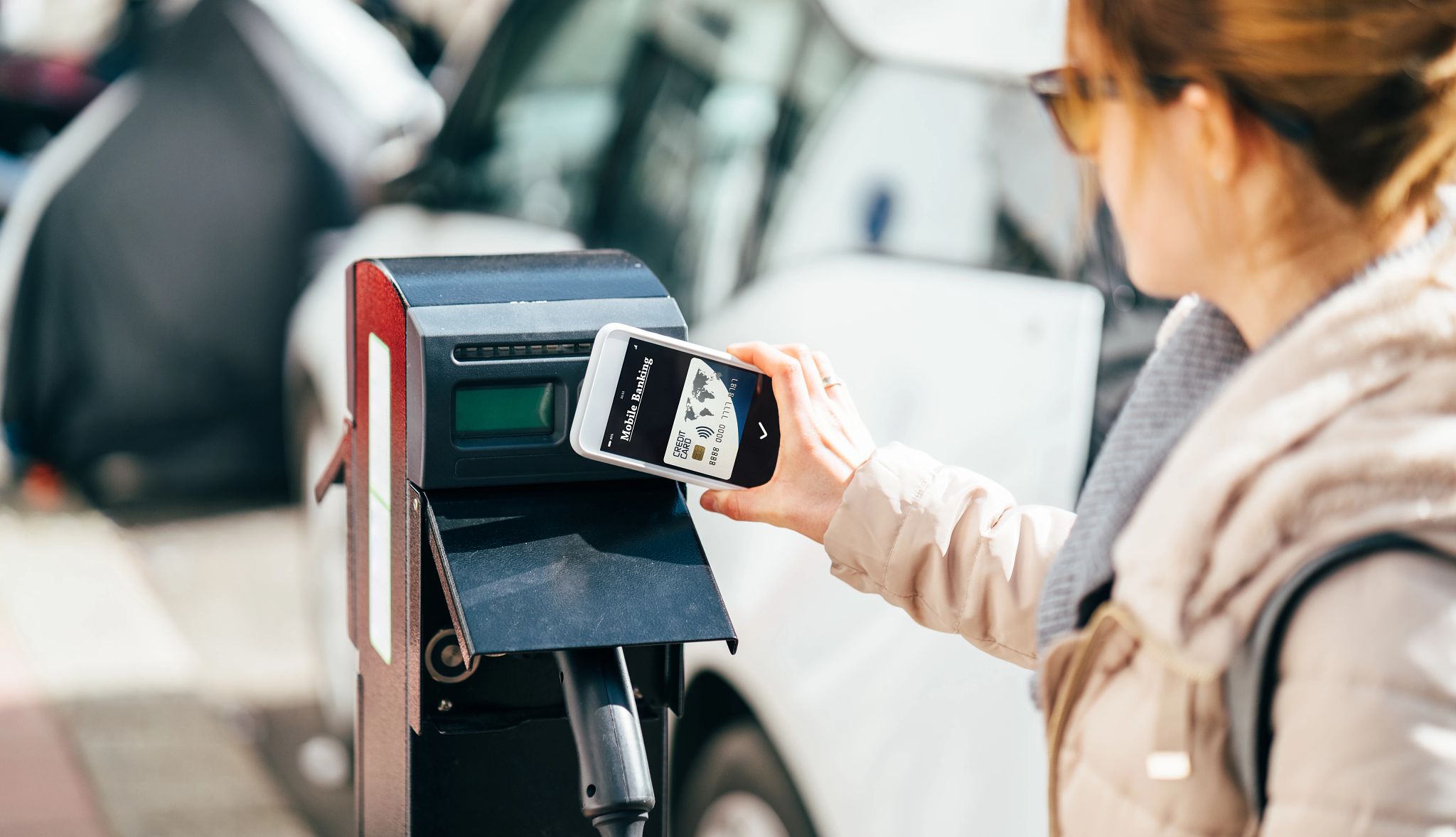 What to understand Woman holding cellular phone with mobile banking card on screen up to vehicle charging station