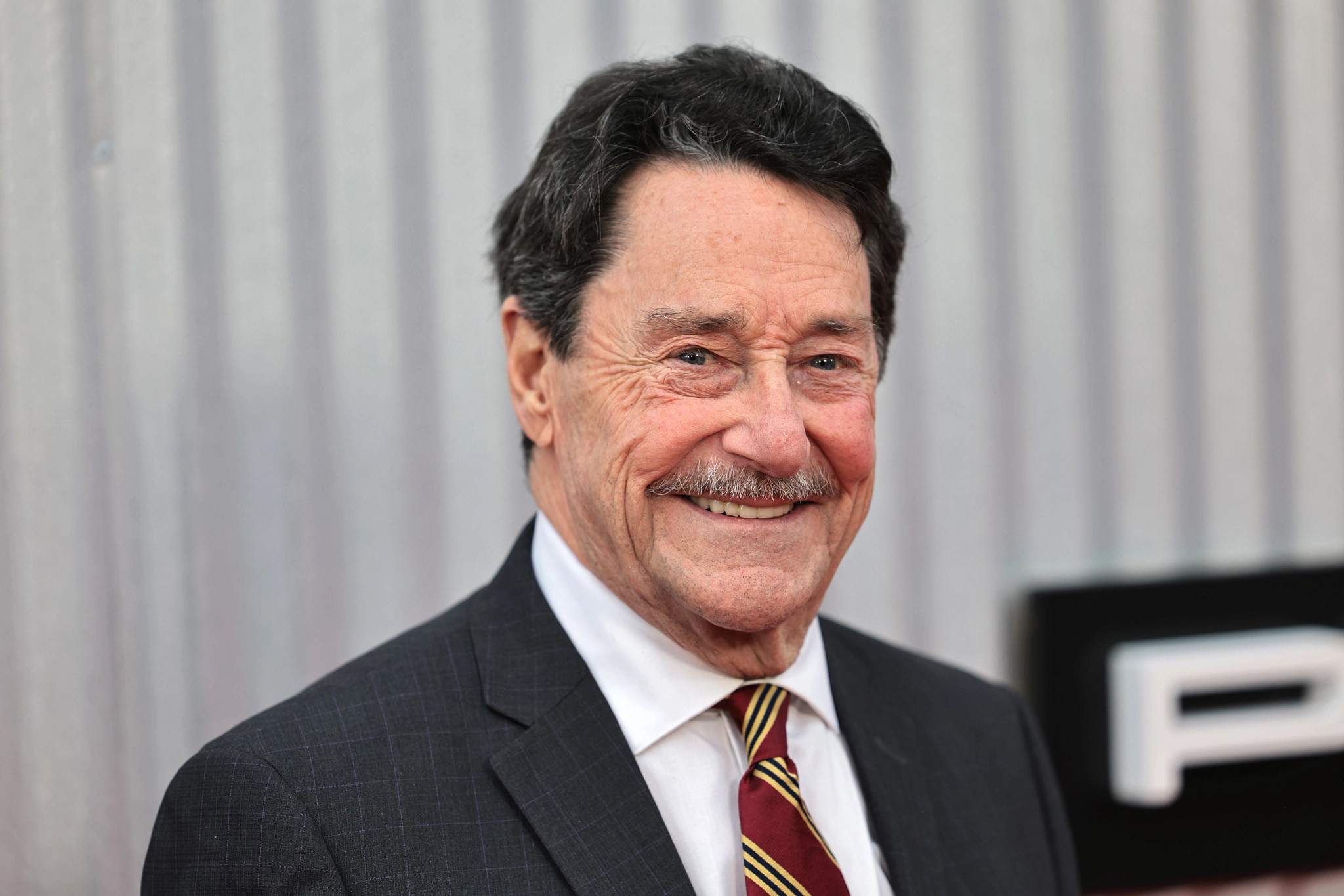 Peter Cullen smiling, wearing a suit jacket and tie