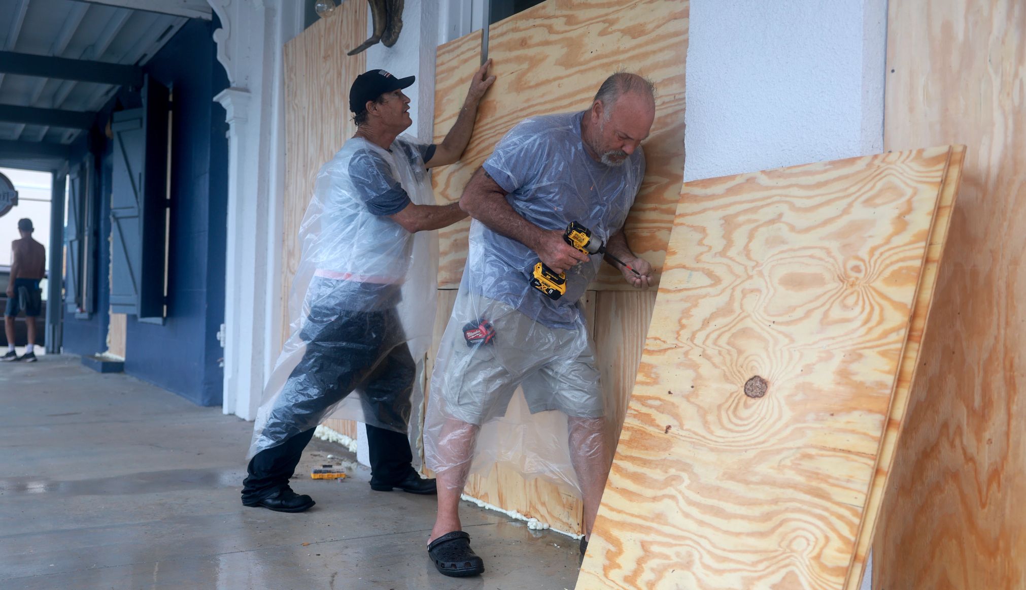 dos hombres colocan maderas contrachapadas sobre las ventanas de un local comercial en Florida