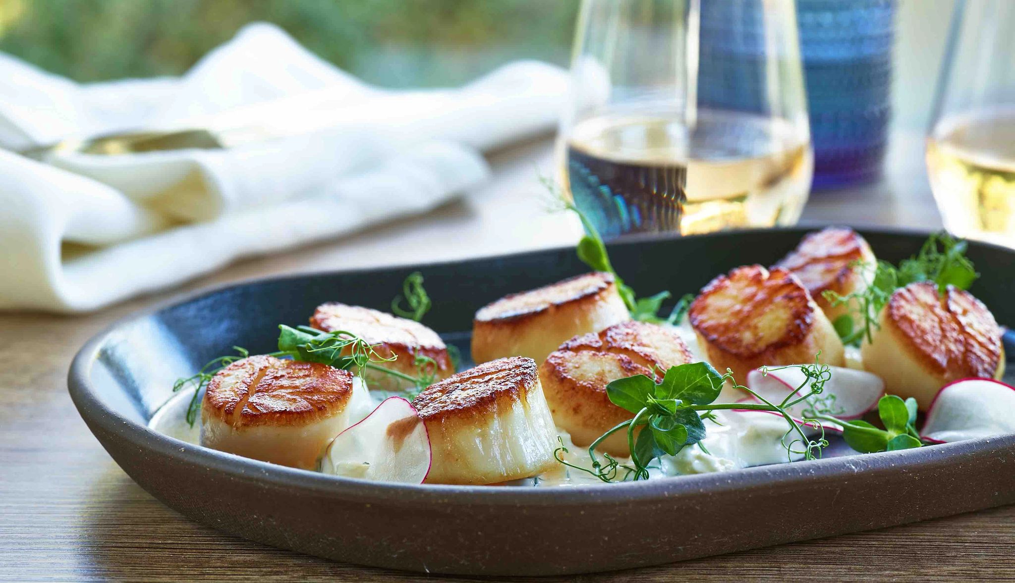 Seared scallops with tzatziki Seared scallops in dish on table with glass of white wine behind it