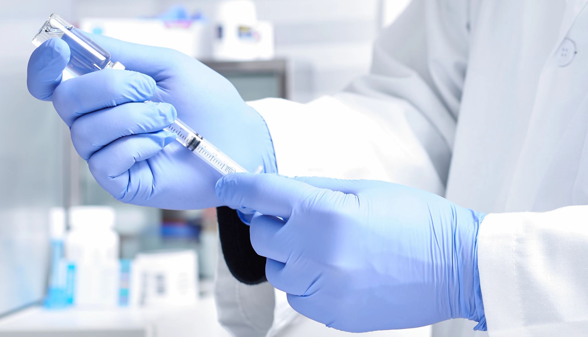 Medical Matters Hands wearing protective gloves, dialing medicine into syringe from a vaccine vial