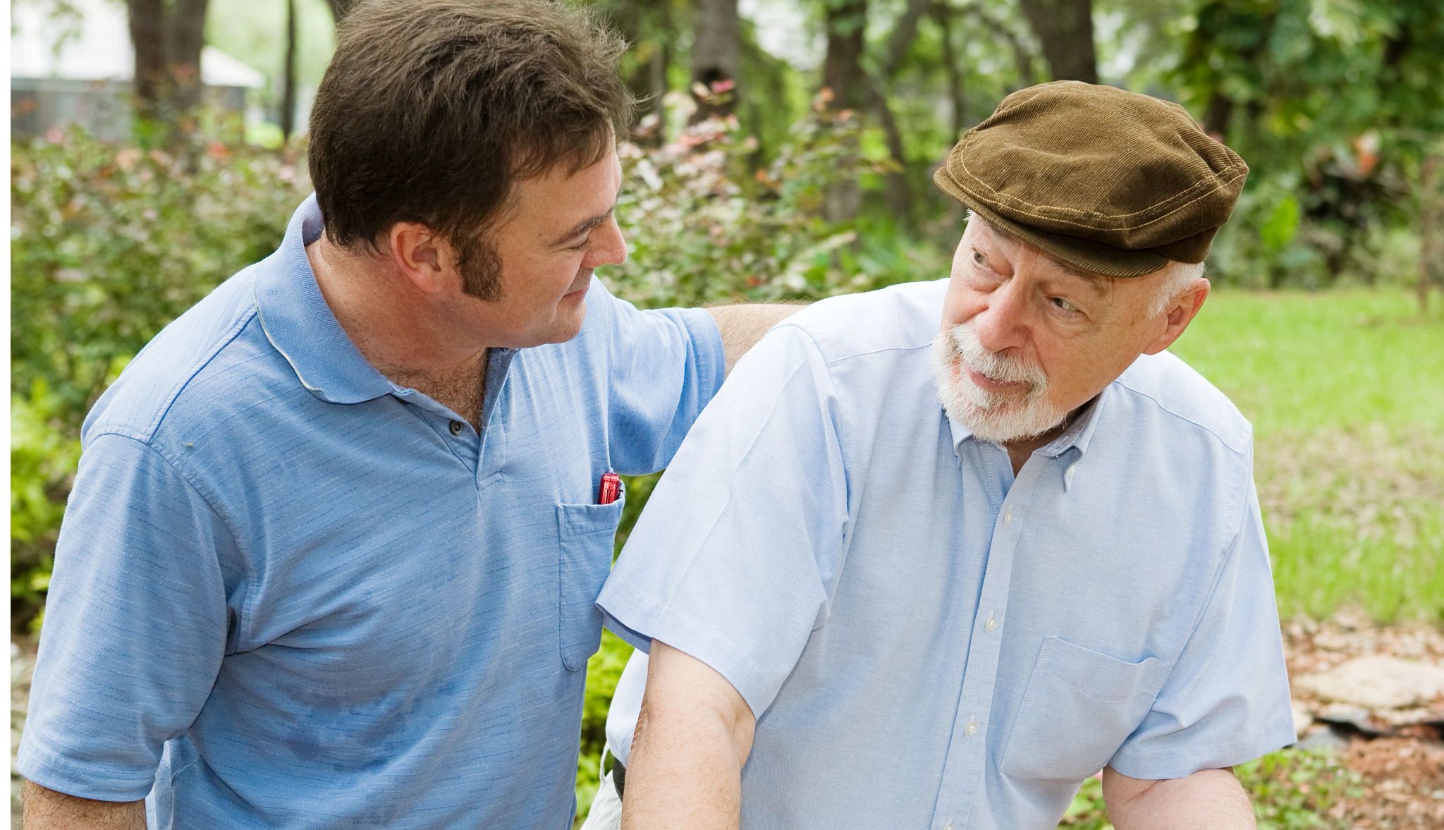 A middle-aged man helping an older man with a walker outside. A middle-aged man helping an older man with a walker outside.